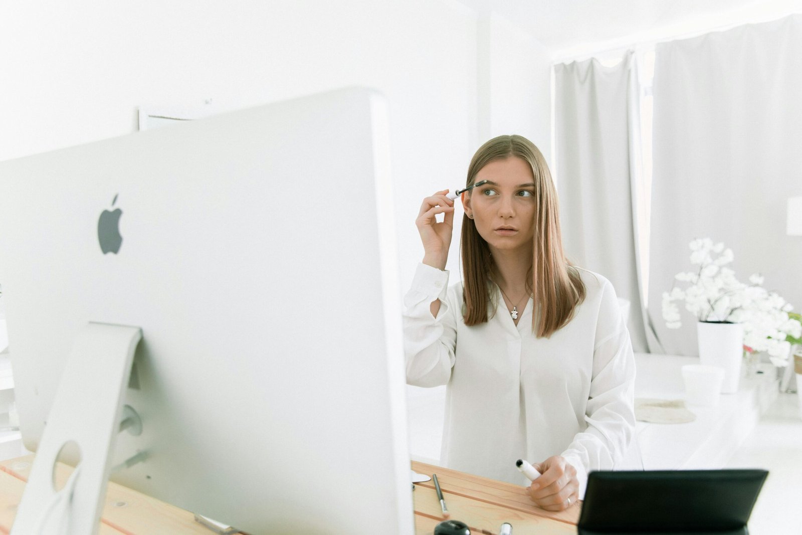 Woman applying makeup in front of computer, blending self-care with technology.