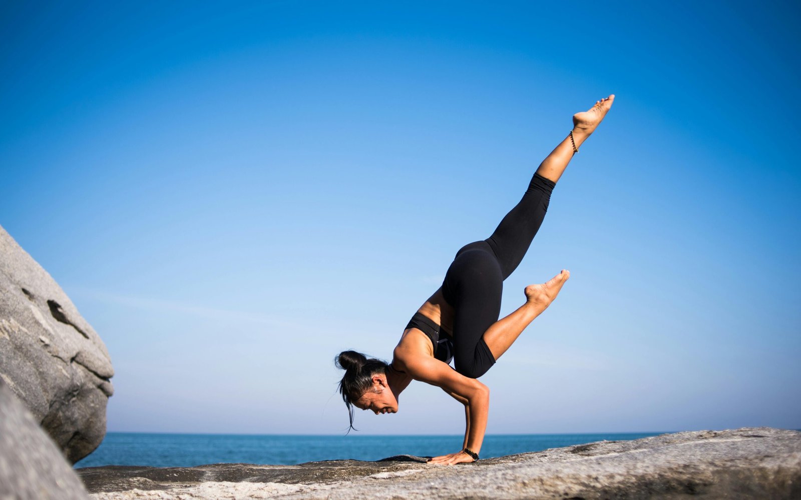 pexels-photo-317157-317157 Woman performing a yoga pose on a rocky beach with ocean view and clear blue sky.